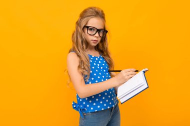 Gözlük ve defterle turuncu arka planda poz veren küçük akıllı kız.  