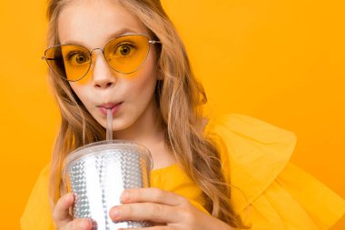 Turuncu arka planda kağıt bardakla poz veren sevimli küçük kız. 