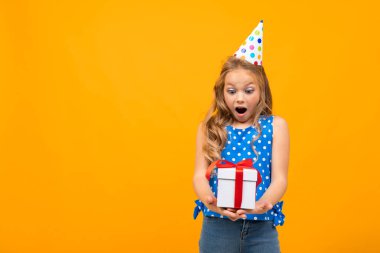 Küçük akıllı kız turuncu arka planda hediyeyle poz veriyor.  