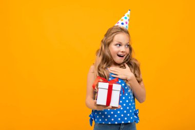 Küçük akıllı kız turuncu arka planda hediyeyle poz veriyor.  