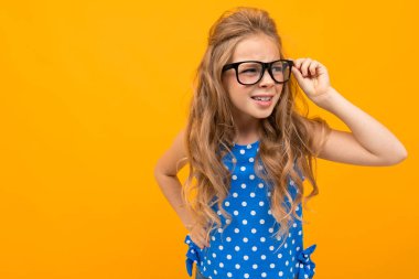 Küçük akıllı kız gözlükleriyle turuncu arka planda poz veriyor.  