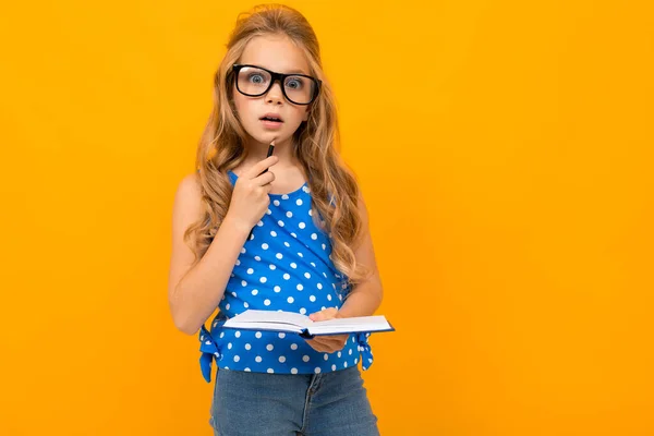 Liten Smart Flicka Poserar Med Glasögon Och Anteckningsbok Mot Orange — Stockfoto