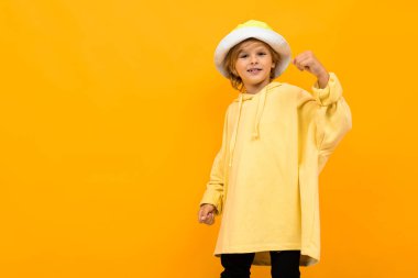 Kapüşonlu ve şapkalı şık çocuk turuncuya karşı poz veriyor. 