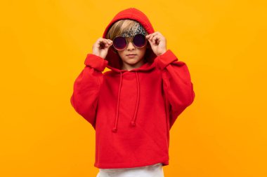 Kırmızı kapüşonlu ve güneş gözlüklü yakışıklı çocuk turuncuya karşı poz veriyor. 