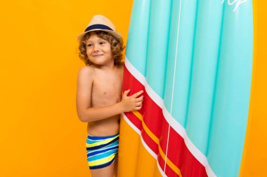 Küçük çocuk turuncu arka planda sahilde poz veriyor. 