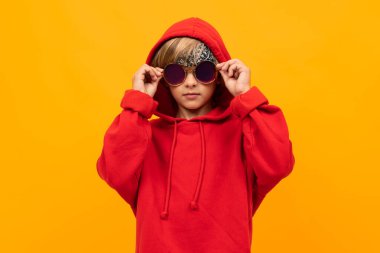 Kırmızı kapüşonlu ve güneş gözlüklü yakışıklı çocuk turuncuya karşı poz veriyor. 