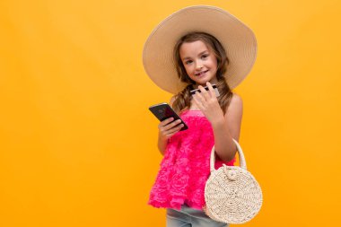 Küçük kız cep telefonu ve kredi kartıyla turuncu arka planda poz veren bayan gibi. 