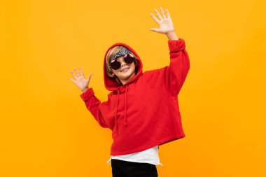 Kırmızı kapüşonlu ve güneş gözlüklü yakışıklı çocuk turuncuya karşı poz veriyor. 