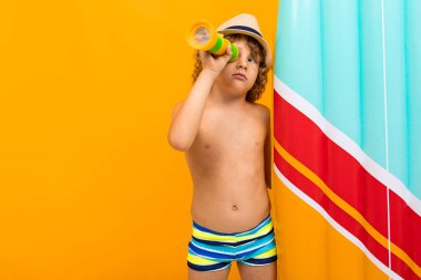 Küçük çocuk turuncu arka planda sahilde poz veriyor. 