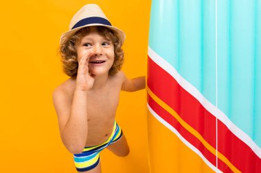 Küçük çocuk turuncu arka planda sahilde poz veriyor. 