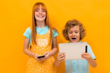 Kızıl saçlı güzel bir kız ve turuncu arka planda poz veren küçük bir oğlan. 