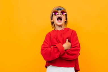 Kırmızı kapüşonlu ve güneş gözlüklü yakışıklı çocuk turuncuya karşı poz veriyor. 