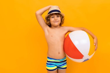 Küçük çocuk turuncu arka planda sahilde poz veriyor. 