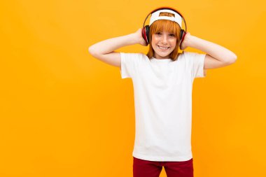 Turuncu arka planda kulaklıkla poz veren sevimli kızıl kız.