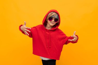 Kırmızı kapüşonlu ve güneş gözlüklü yakışıklı çocuk turuncuya karşı poz veriyor. 