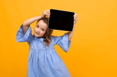 Tabletle turuncu arka planda poz veren sevimli küçük bir kız. 