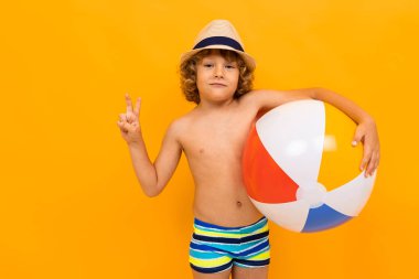 Küçük çocuk turuncu arka planda sahilde poz veriyor. 