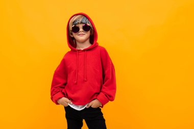Kırmızı kapüşonlu ve güneş gözlüklü yakışıklı çocuk turuncuya karşı poz veriyor. 
