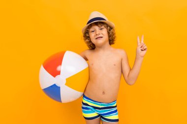 Küçük çocuk turuncu arka planda sahilde poz veriyor. 