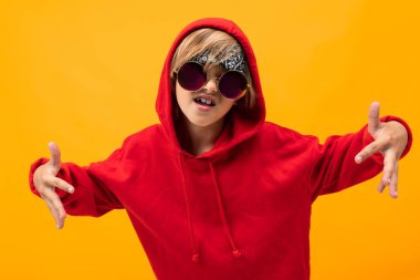 Kırmızı kapüşonlu ve güneş gözlüklü yakışıklı çocuk turuncuya karşı poz veriyor. 