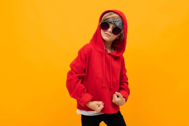Kırmızı kapüşonlu ve güneş gözlüklü yakışıklı çocuk turuncuya karşı poz veriyor. 