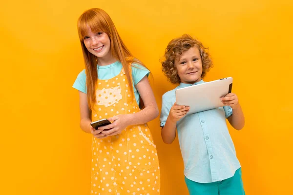 Pretty teenage girl with red hair and little boy posing against orange background