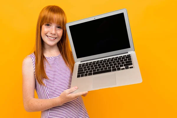 Turuncu Arka Planda Dizüstü Bilgisayarı Olan Kızıl Tatlı Bir Kız — Stok fotoğraf