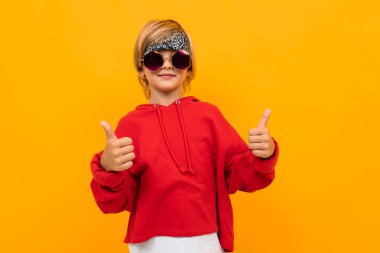 Kırmızı kapüşonlu ve güneş gözlüklü yakışıklı çocuk turuncuya karşı poz veriyor. 