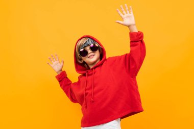 Kırmızı kapüşonlu ve güneş gözlüklü yakışıklı çocuk turuncuya karşı poz veriyor. 