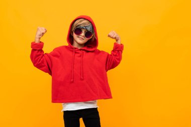Kırmızı kapüşonlu ve güneş gözlüklü yakışıklı çocuk turuncuya karşı poz veriyor. 