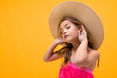 Hasır şapkalı, turuncu arka planda poz veren güzel duygusal küçük kız. 