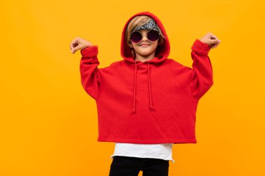 Kırmızı kapüşonlu ve güneş gözlüklü yakışıklı çocuk turuncuya karşı poz veriyor. 