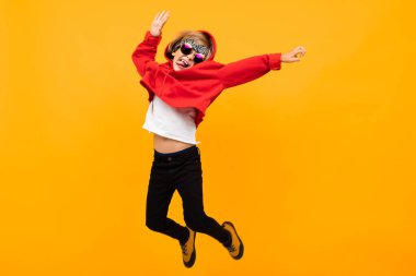 Kırmızı kapüşonlu ve güneş gözlüklü yakışıklı çocuk turuncuya karşı poz veriyor. 