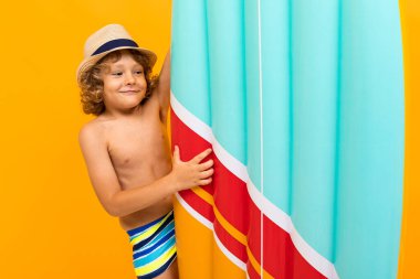 Küçük çocuk turuncu arka planda sahilde poz veriyor. 