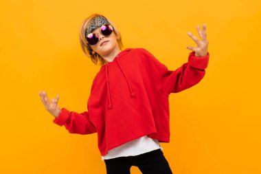 Kırmızı kapüşonlu ve güneş gözlüklü yakışıklı çocuk turuncuya karşı poz veriyor. 