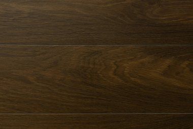 Koyu ahşap bir zeminin yakın plan görüntüsü zengin ve pürüzsüz tahıllar içeriyor. Ayar iyi aydınlatılmış, çağdaş bir uzayda materyalin zarafetini gösteriyor..