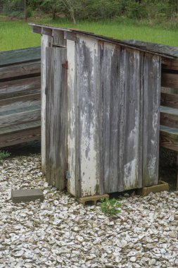 Eski, yıpranmış, ahşap bir tuvalet, yerde istiridye kabuklarıyla kaplı..
