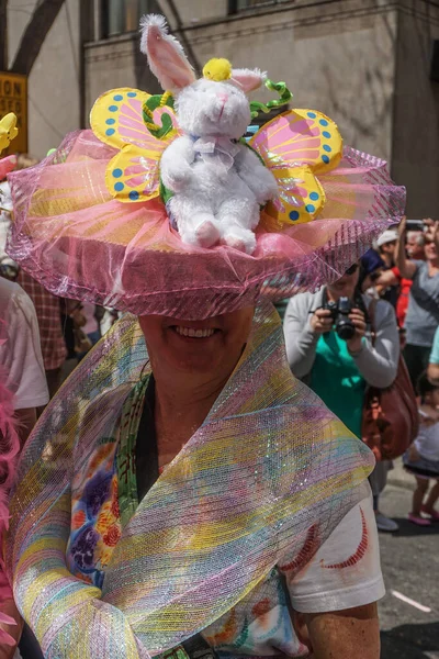 在一年一度的第五大道复活节游行中 一位面带微笑的女士戴着一顶精致的复活节帽子 上面有一只毛绒绒兔子和一只蝴蝶 — 图库照片