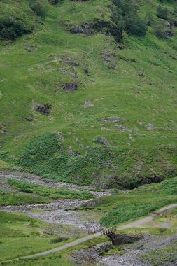 Bidean Nam Bian 'ın eteklerinde bir yaya köprüsü İskoçya' nın dağlık kesimlerinde Glen Coe 'nun Üç Kız Kardeşi' nin yanında Glen Coe kadar uzanan dik tepeler..