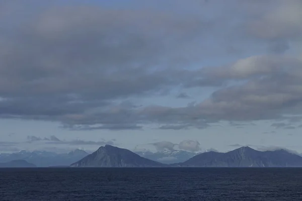 Islands and distant snow-capped mountains viewed from a cruise ship in the Gulf of Alaska, on a misty morning at sea.