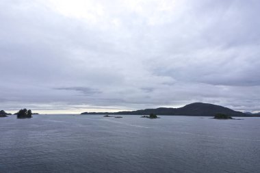 Sitka, Alaska, ABD: Ufuktaki şafak ve doğu kanalının üzerindeki gökyüzünde yoğun bulutlar, adalar ve uzakta küçük tekneler.