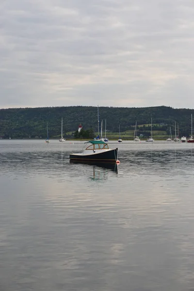 カナダ ノバスコシア州バデッキ ケープ ブレトン島のブラス ドール湖に停泊する小型ボートで 背景にはキドストン島灯台 1912年 がある — ストック写真