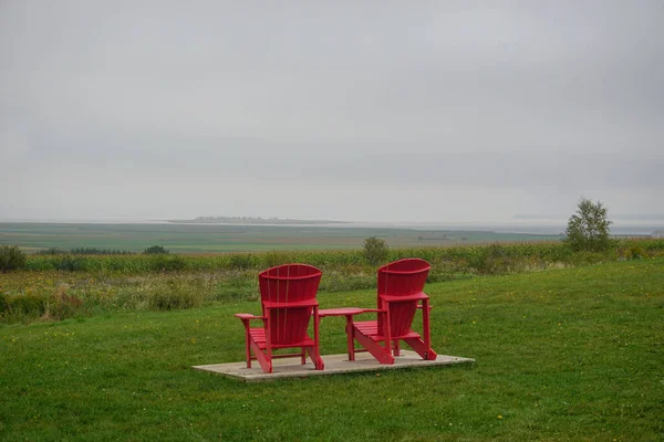Kings County, Nova Scotia, Canada: Two red Adirondacks chairs facing the Minas Basin at the Grand-Pre National Historic Site, on a cloudy summer day.