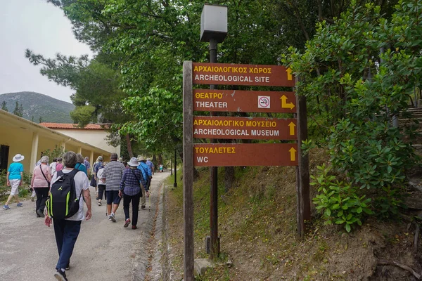 Yunanistan 'ın Epidaurus kenti: Peloponnese' de bir arkeoloji sahası olan Epidaurus 'ta turistler Yunanca ve İngilizce tabelaların önünden geçtiler.