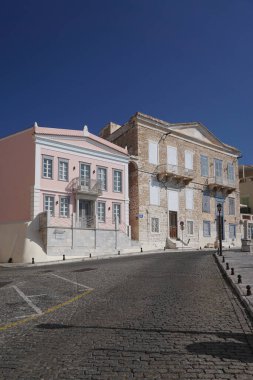 Hermoupolis, Syros, Yunanistan: Ege adası Syros 'ta, Ermoupoli' de (Hermoupolis) bir kaldırım taşı caddesinde, derin mavi gökyüzü altında pastel binalar.