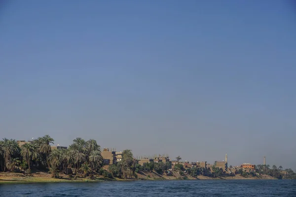 Nile River, Egypt: Houses, date palm trees, and a minaret along the east bank of the Nile River.