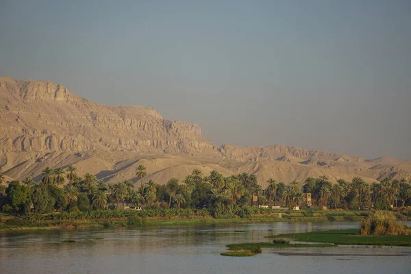 Nile River, Egypt: Houses and date palm trees along the west bank of the Nile; large sand dunes in the background; marshy islands in the foreground.