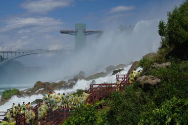 Niagara Şelalesi, New York: Sarı yağmurluklu turistler, Keçi Adası 'ndaki Rüzgâr Mağarası' nın, merdivenlerin ve platformların keyfini çıkarıyorlar..