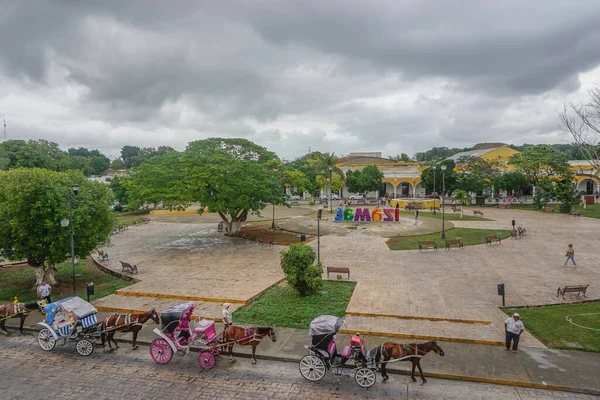 Izamal, Yucatan, Meksika: Atlar ve arabalar Izamal 'ın ana meydanı boyunca bulutlu bir gökyüzünün altında yolcuları bekliyorlar.