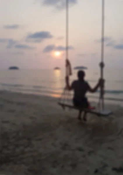 Gün batımında plajda salıncakta oynayan bulanık bir kadın..